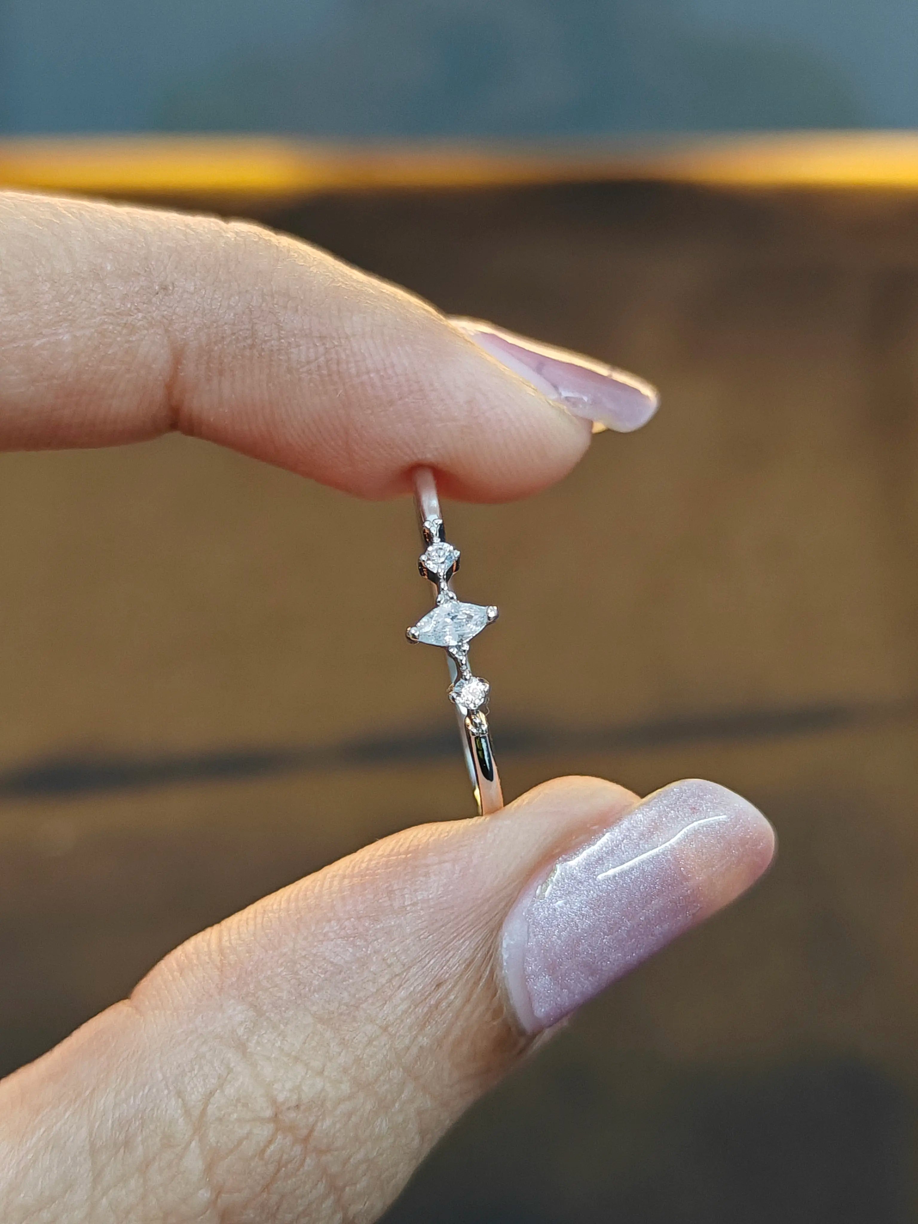 Silver earring with small diamonds held between fingers against a blurred background